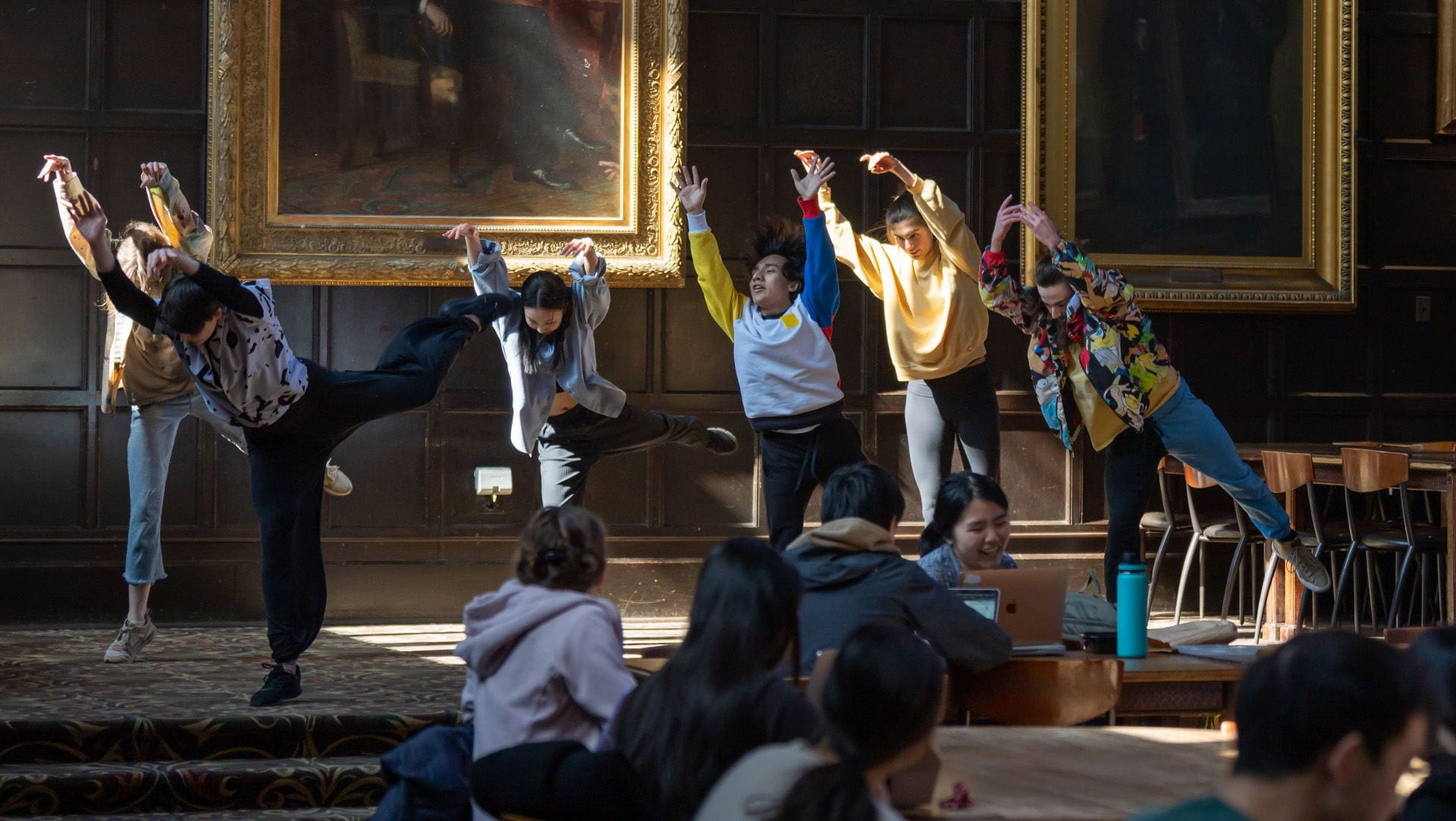 Six students reach upwards during a dance performance in a wood paneled room