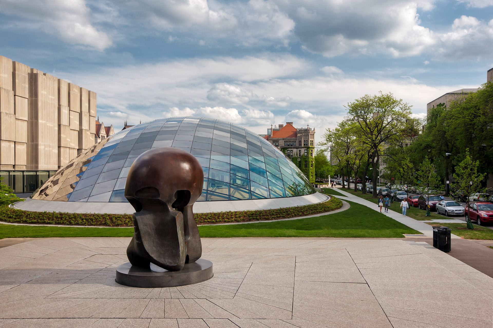 A bronze, mushroom cloud shaped sculpture in front of a domed glass building