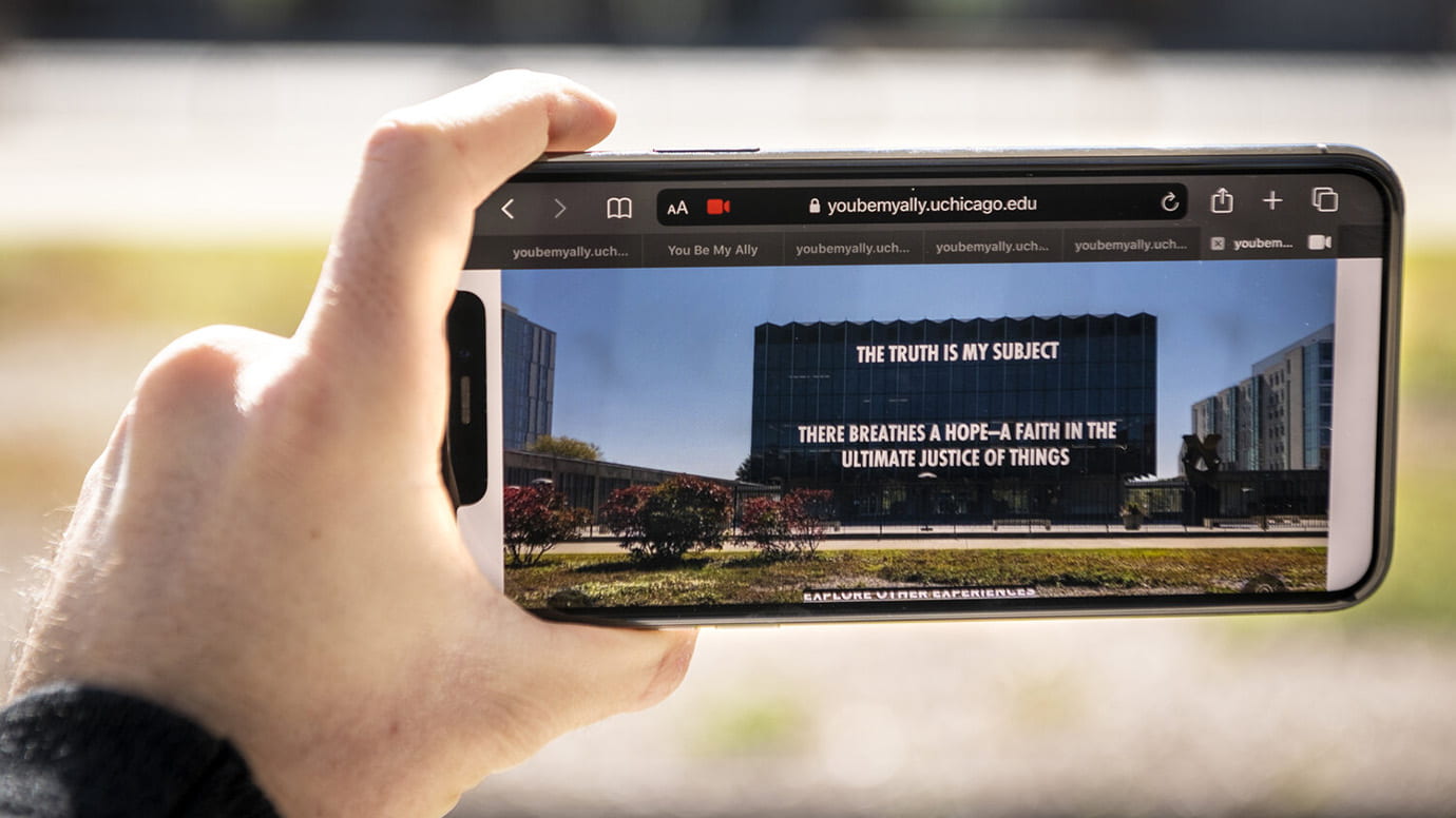 A person's left hand holds up a mobile phone that's displaying a picture of a building with text on it