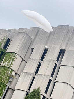 A small cloud disk floats in front of a brutalist building