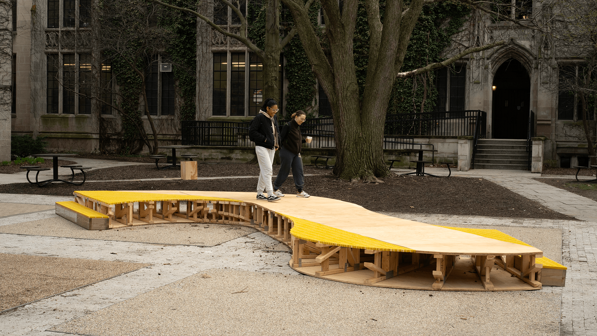 Two people stroll across a low s-shaped platform sculpture